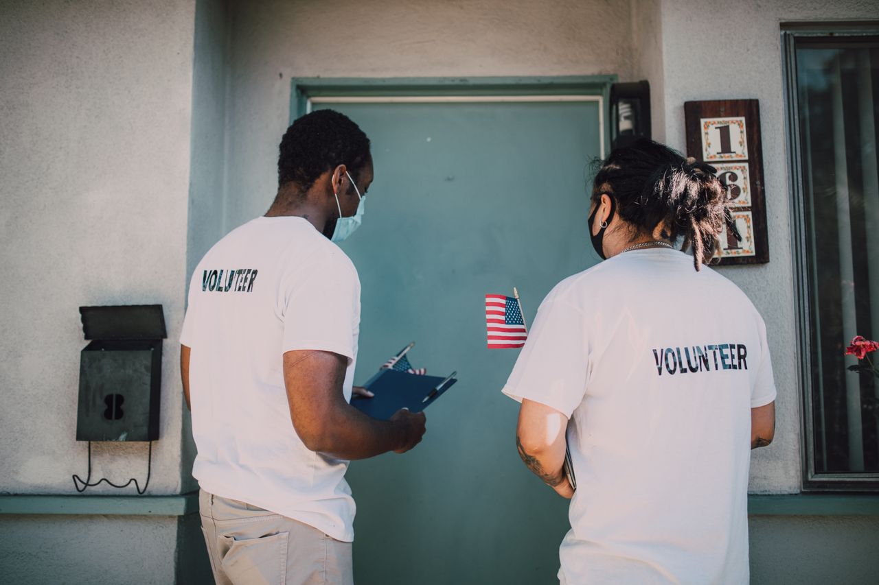 about-01 Two volunteers wear masks and visit community homes, engaging in outreach activities.