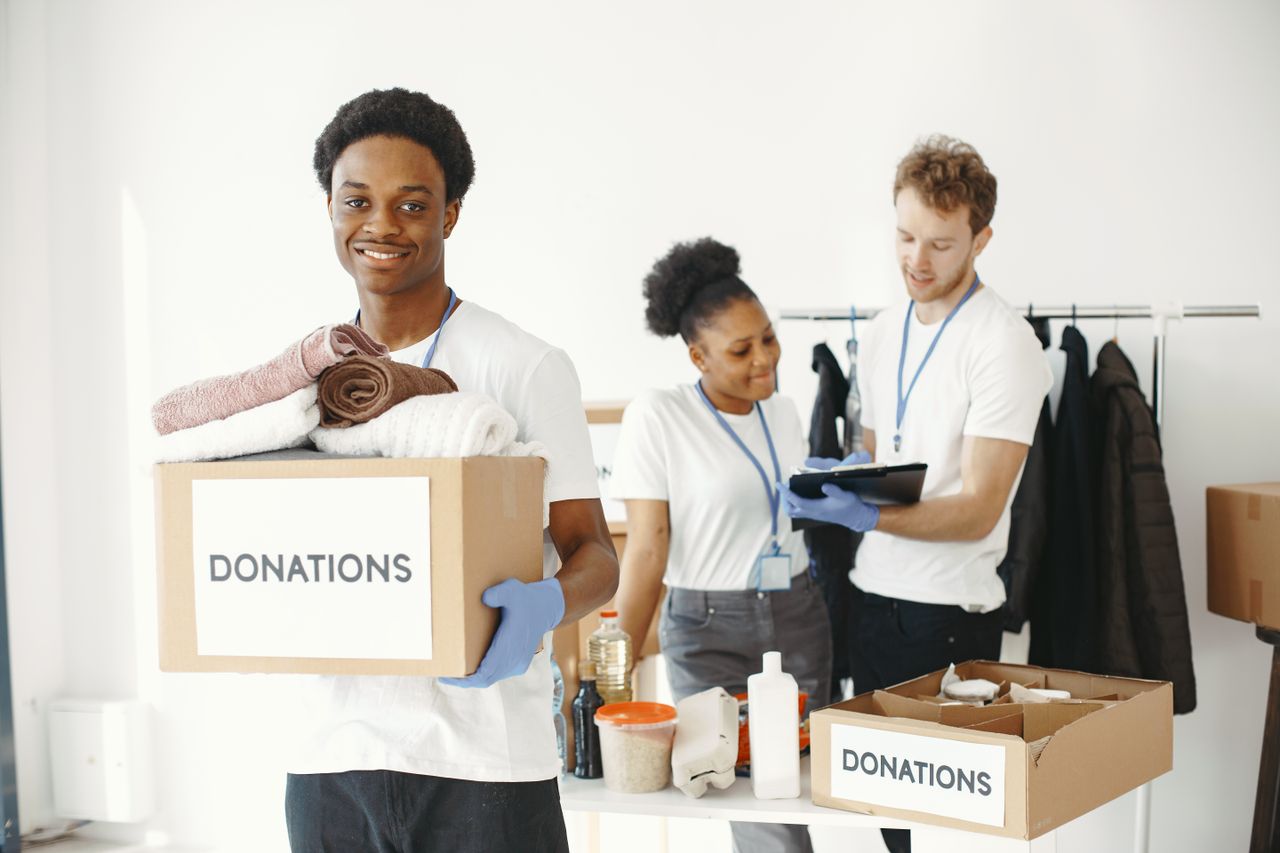 gallery-1 Diverse group of volunteers organizing donation boxes with clothes and supplies indoors.